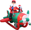 Santa in a pilot cap flying a red and green propeller plane with a penguin behind him