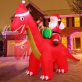 Santa riding a red dinosaur in a Santa hat, inflatable in front of a brick house