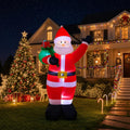 Waving Santa inflatable with a green gift sack in a front yard with a lit Christmas tree