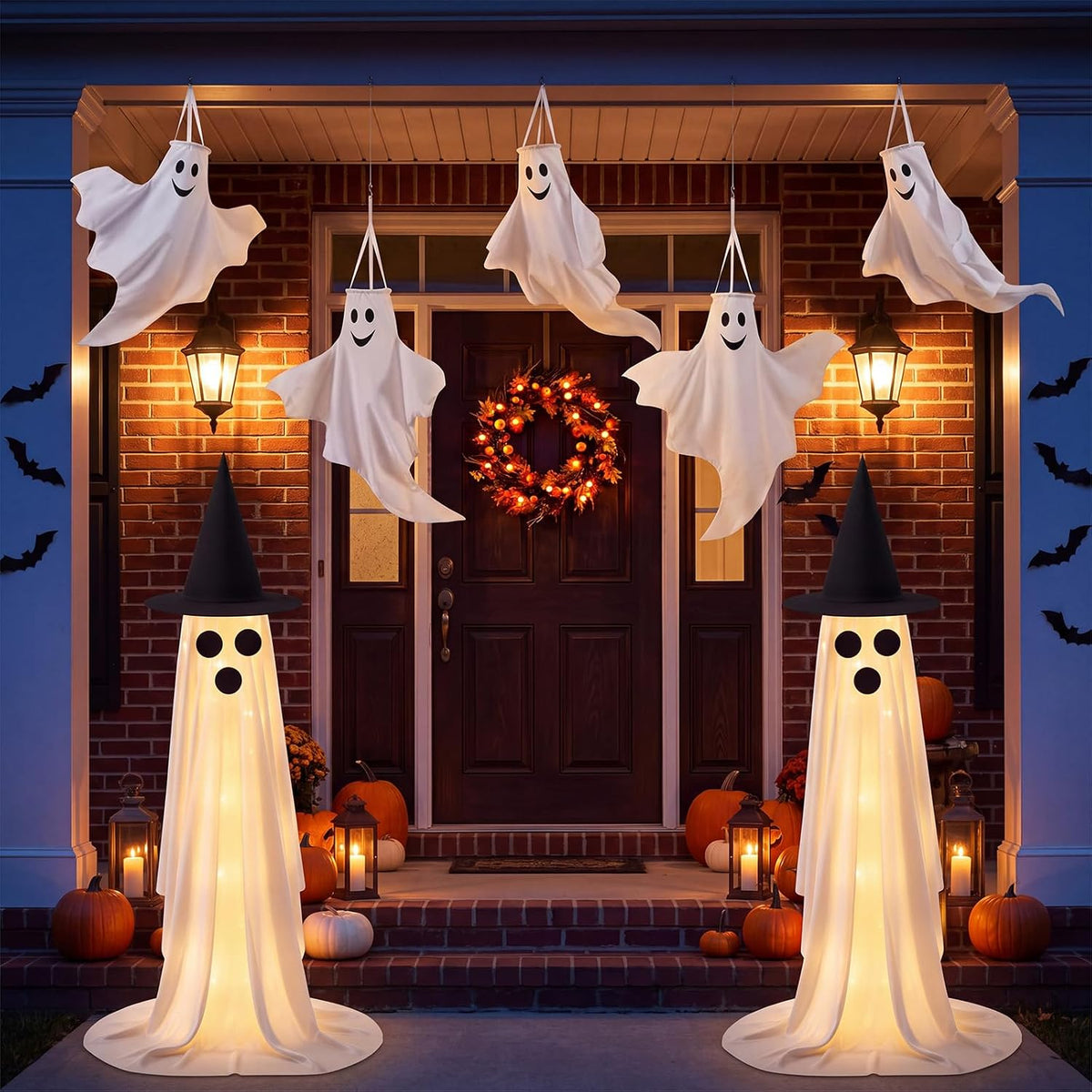 White hanging ghosts on a porch with two glowing standing ghosts in witch hats at the steps