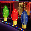 Three large glowing Christmas bulb decorations in green, red and blue on a lawn at night