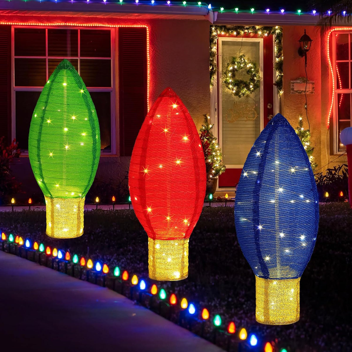 Three large glowing Christmas bulb decorations in green, red and blue on a lawn at night