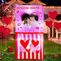 Pink Kissing Booth inflatable with a heart window and red hearts on a lawn with a couple posing inside
