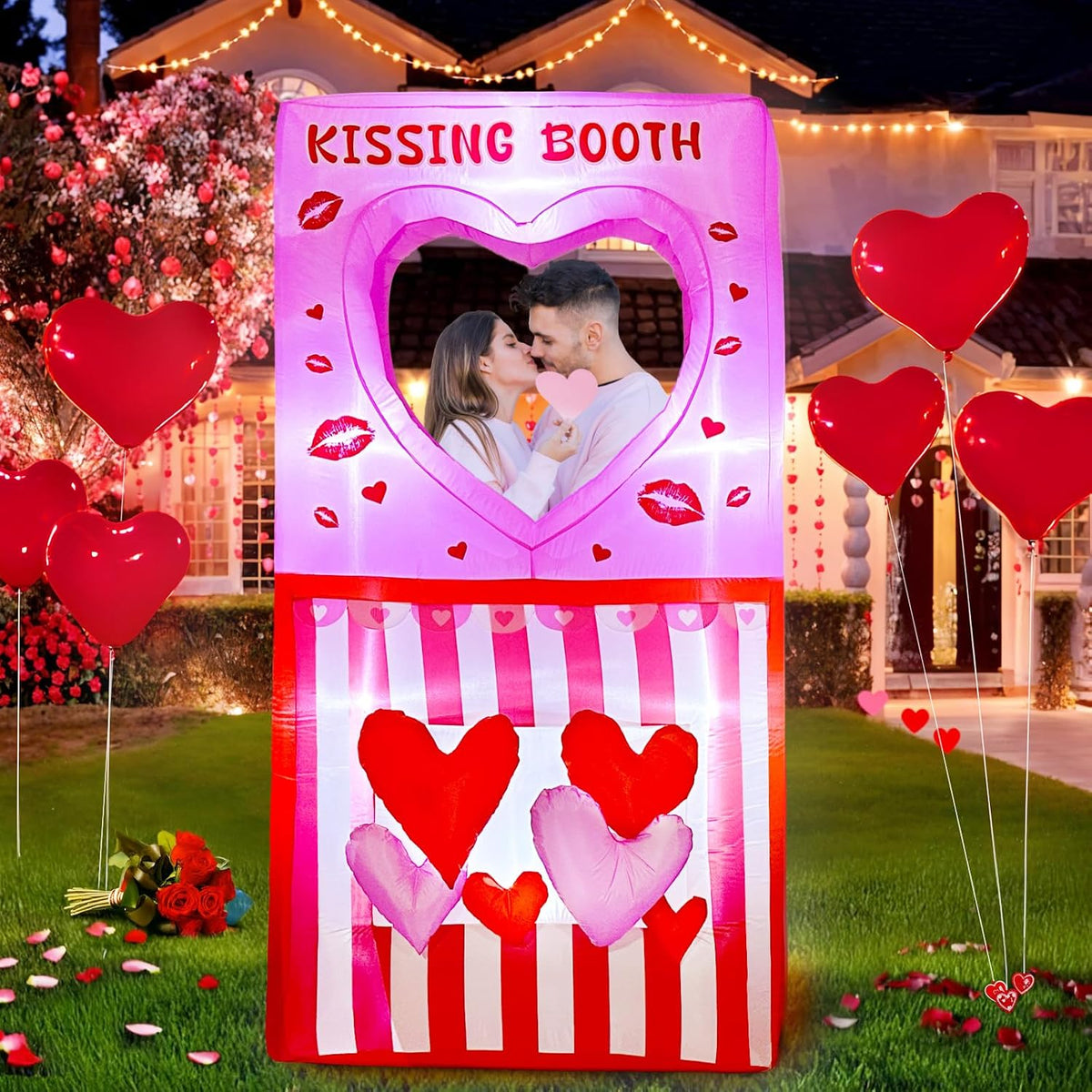 Pink Kissing Booth inflatable with a heart window and red hearts on a lawn with a couple posing inside