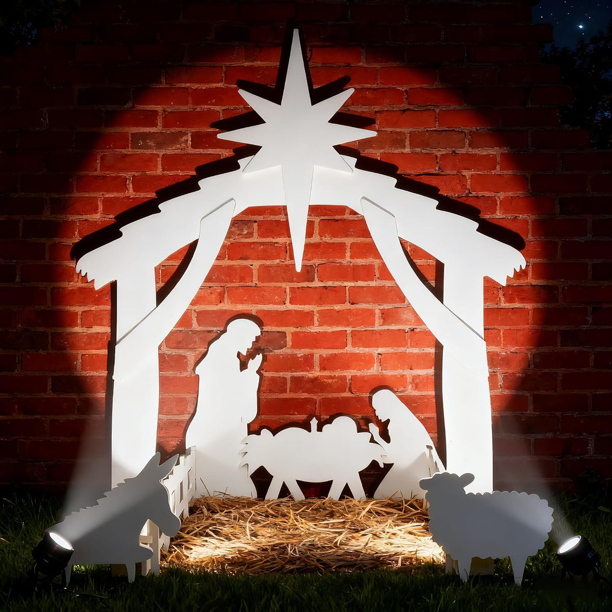 White silhouette nativity scene with a star, the Holy Family, the manger and animals in front of a brick wall